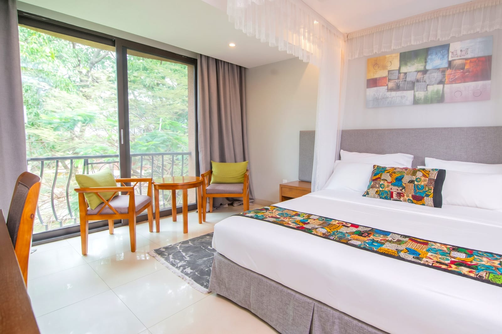 Bright guest room with a canopied bed, African-print throw and a balcony overlooking the trees