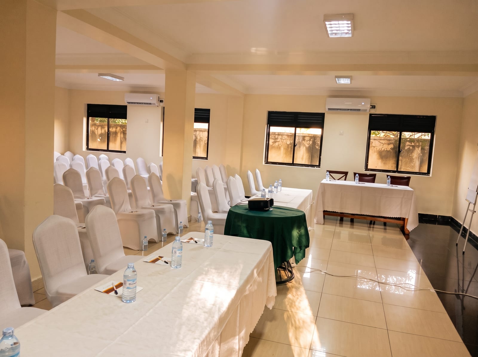 Acholi Inn meeting room set up with a U-shaped table, white chairs and the Acholi Inn logo on the projector screen