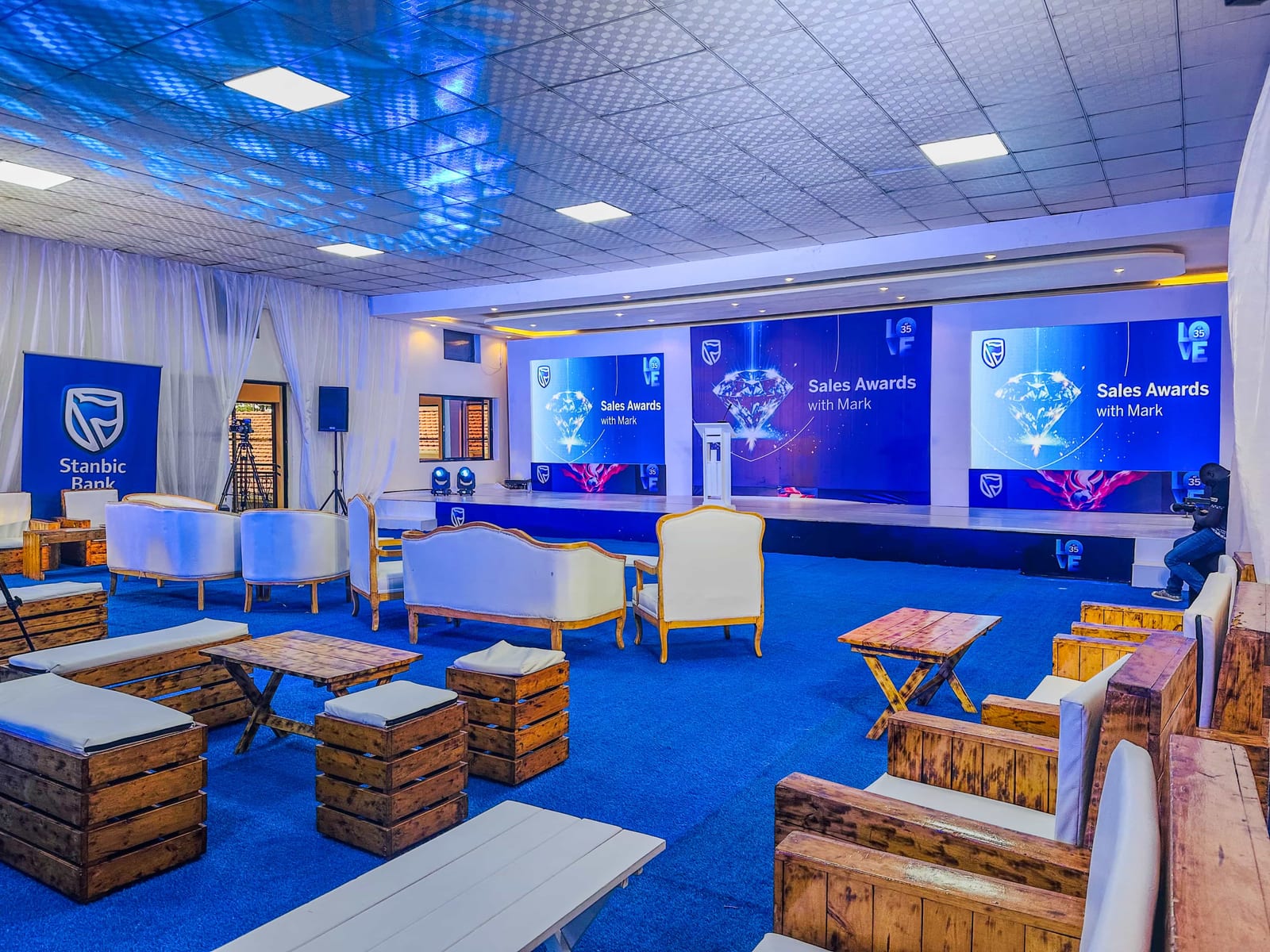 Acholi Inn event hall set up for an awards evening, with a stage, screens and lounge seating on a blue carpet