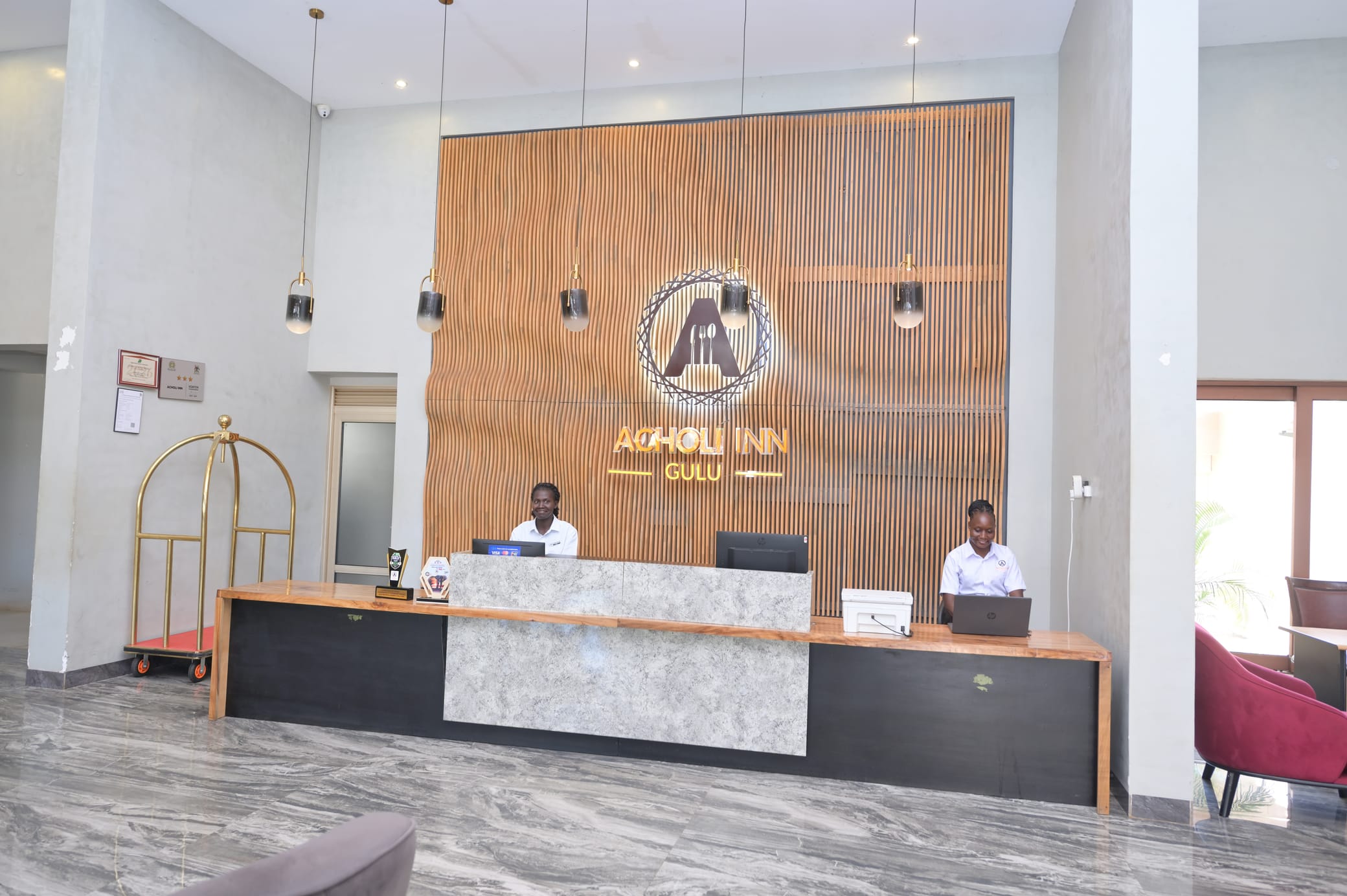 Acholi Inn front desk staff welcoming guests beneath the illuminated Acholi Inn Gulu sign