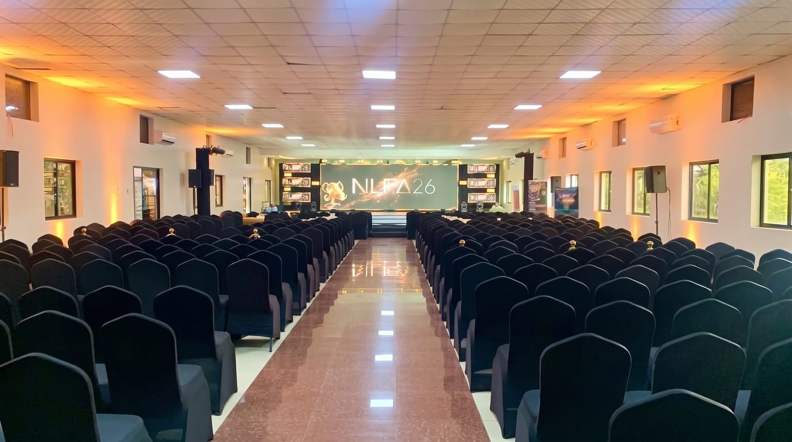 Kidepo Hall set up theatre-style with rows of black-covered chairs facing a stage and large screen