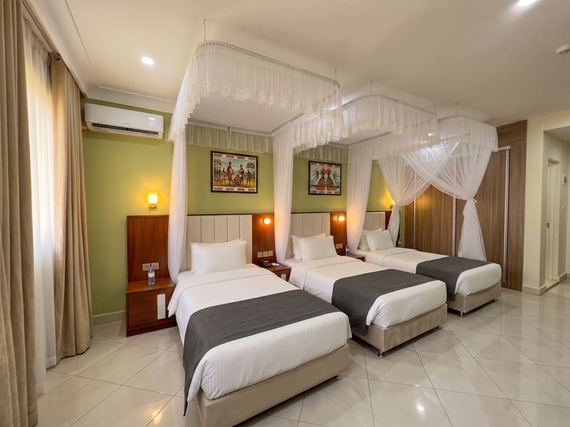 Deluxe Triple Room with three canopied single beds and Acholi artwork